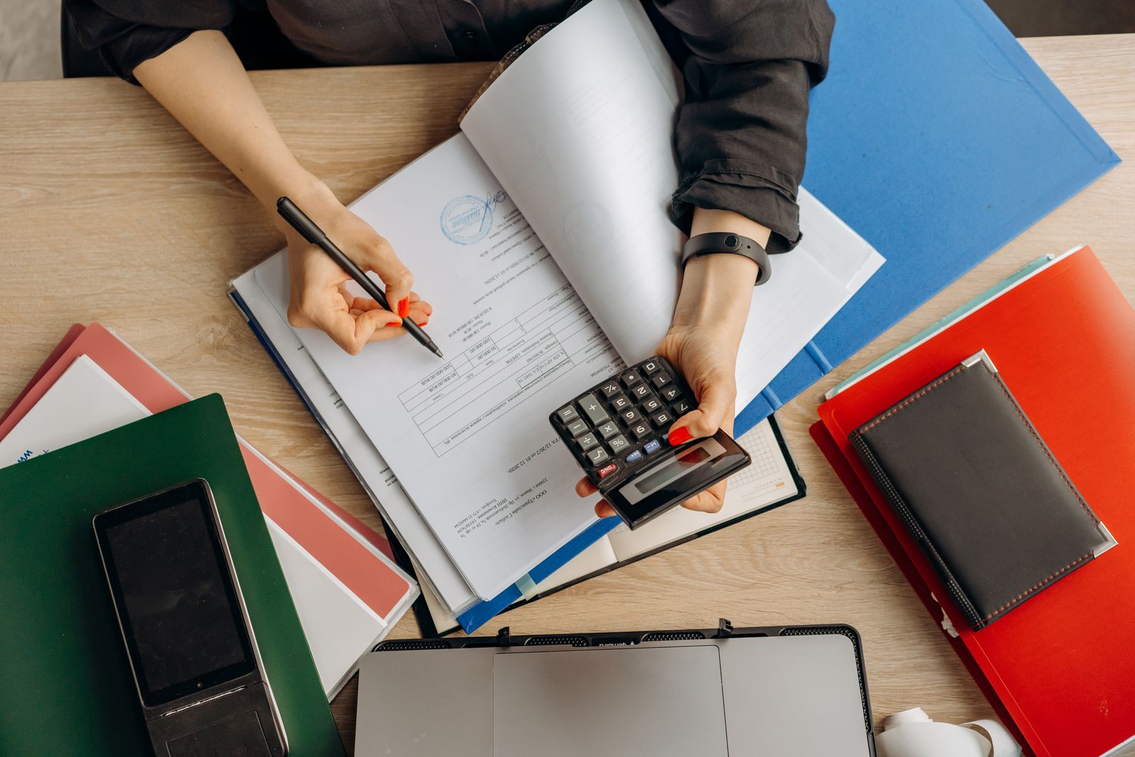 A person reviewing paperwork with a calculator and folders on a desk.